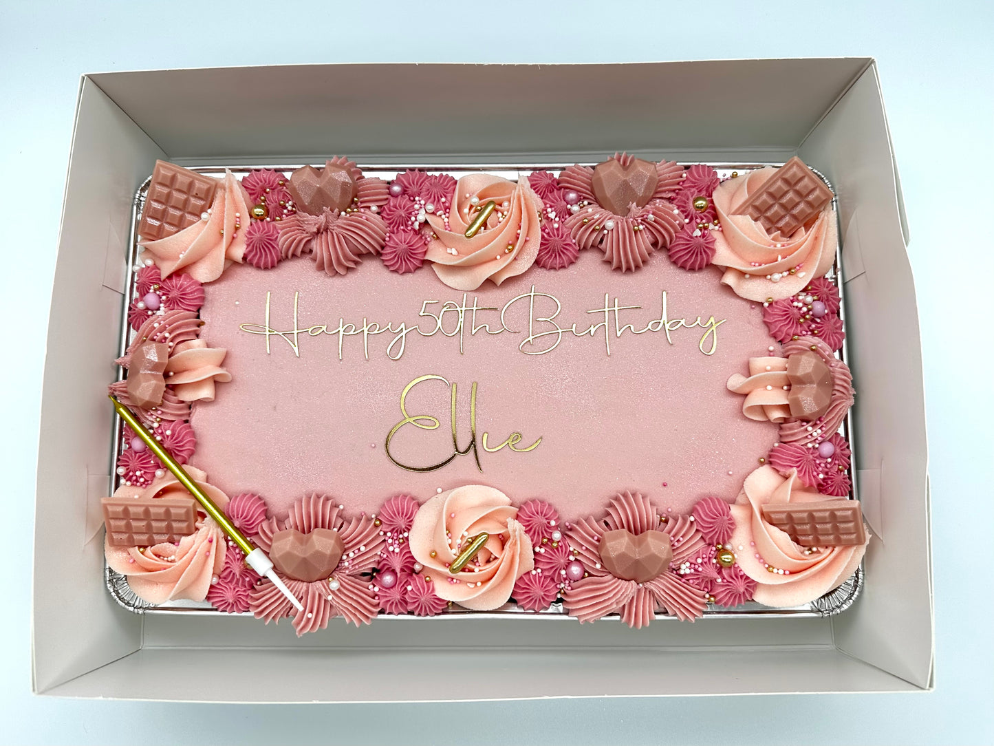 Pink birthday sheet cake with gold lettering, decorated with piped buttercream swirls, edible pearls, gold accents, and chocolate embellishments.